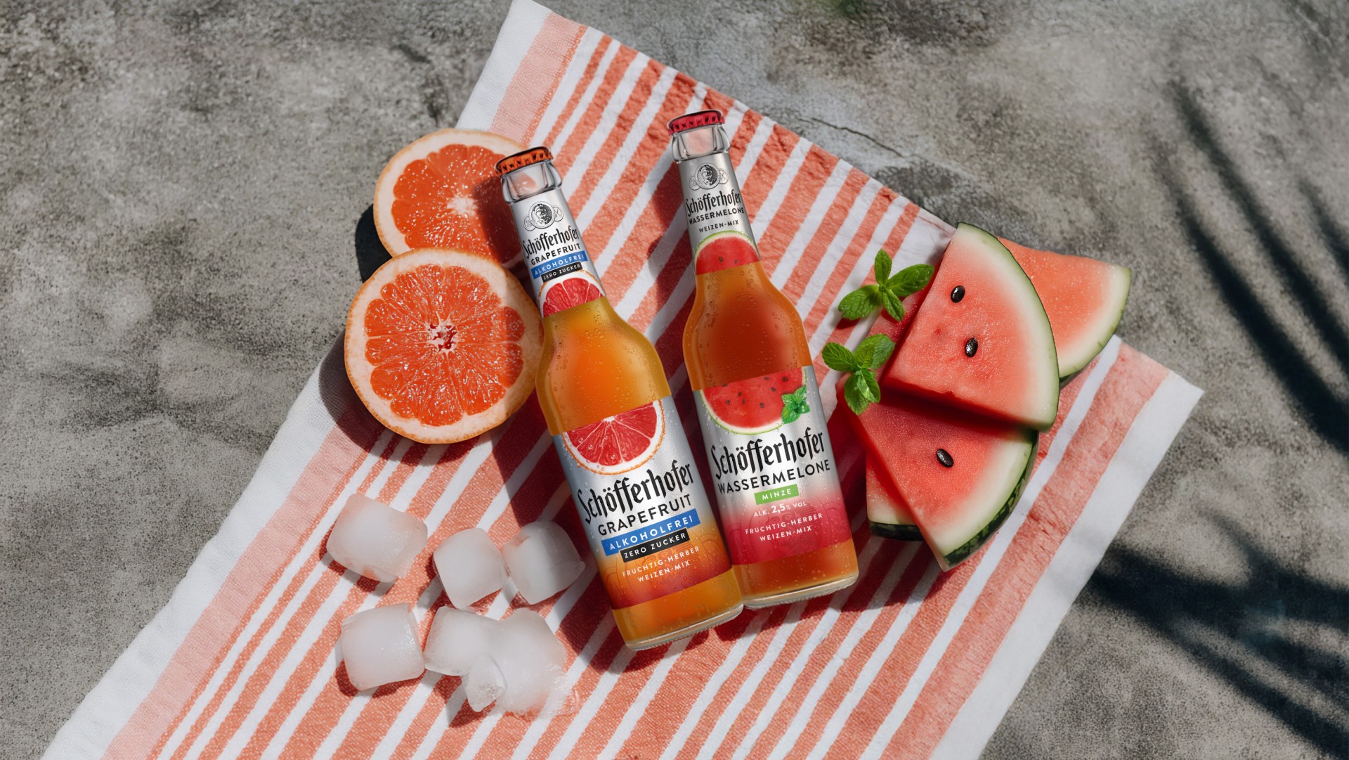 Drei Flaschen Getränk stehen auf Eis, umgeben von einer Grapefruit und Eiswürfeln.