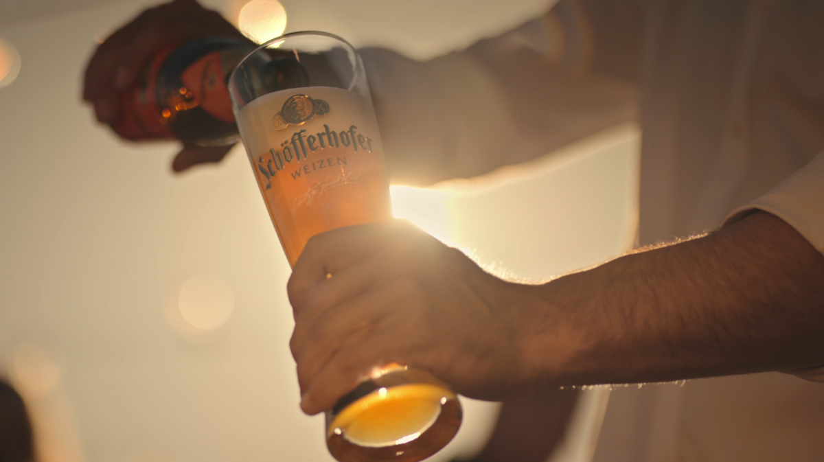 Eine Person füllt ein Weizenglas aus einer Flasche vor einem hellen Licht.