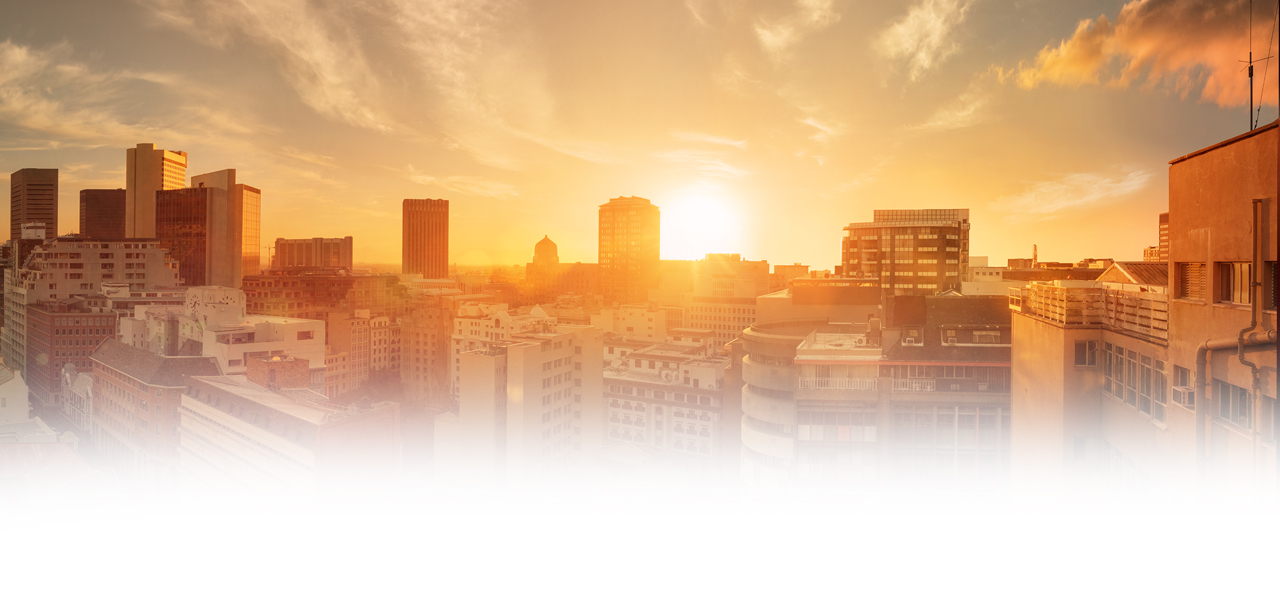 Sonnenaufgang über einer Stadt mit modernen und alten Gebäuden unter einem hellen Himmel.