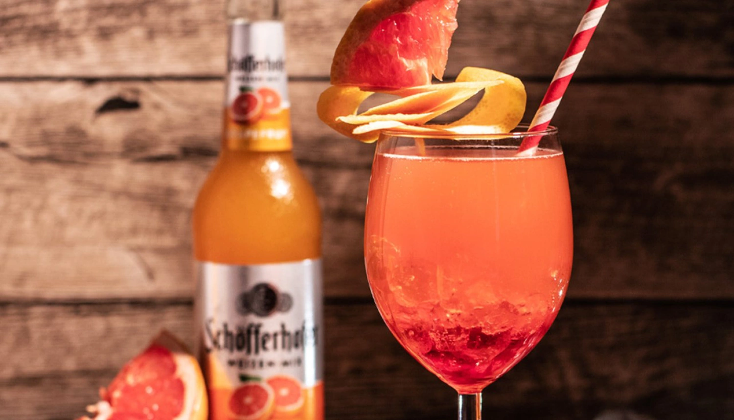 Ein roter Cocktail steht auf einem Holztisch neben einer Flasche mit Zitrusfruchtaufdruck.