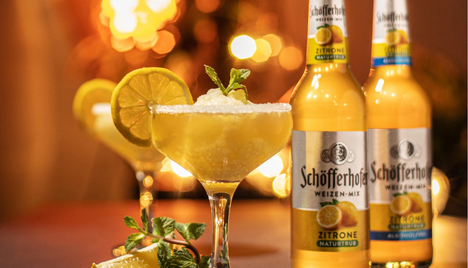 Ein Cocktailglas mit Zitronenscheibe und Minze steht vor zwei Flaschen Getränk.
