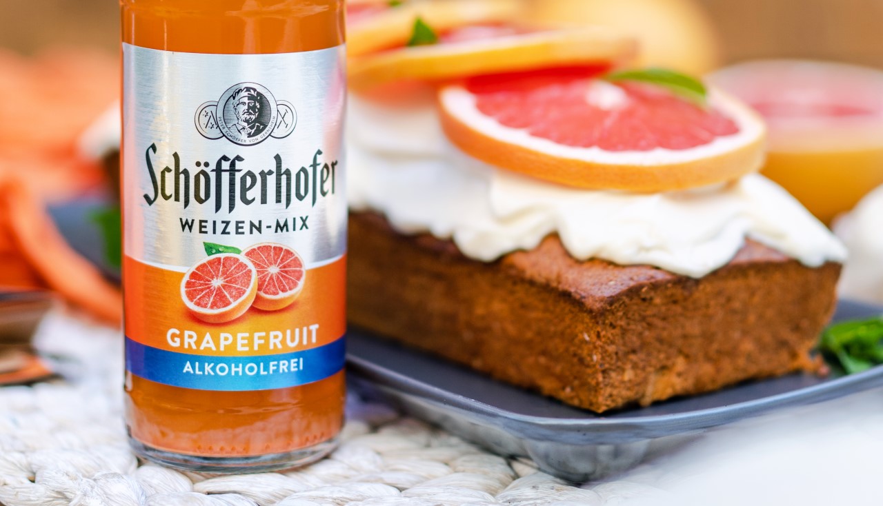 Eine alkoholfreie Getränkeflasche steht neben einem Kuchen mit Frosting und Grapefruitscheiben.