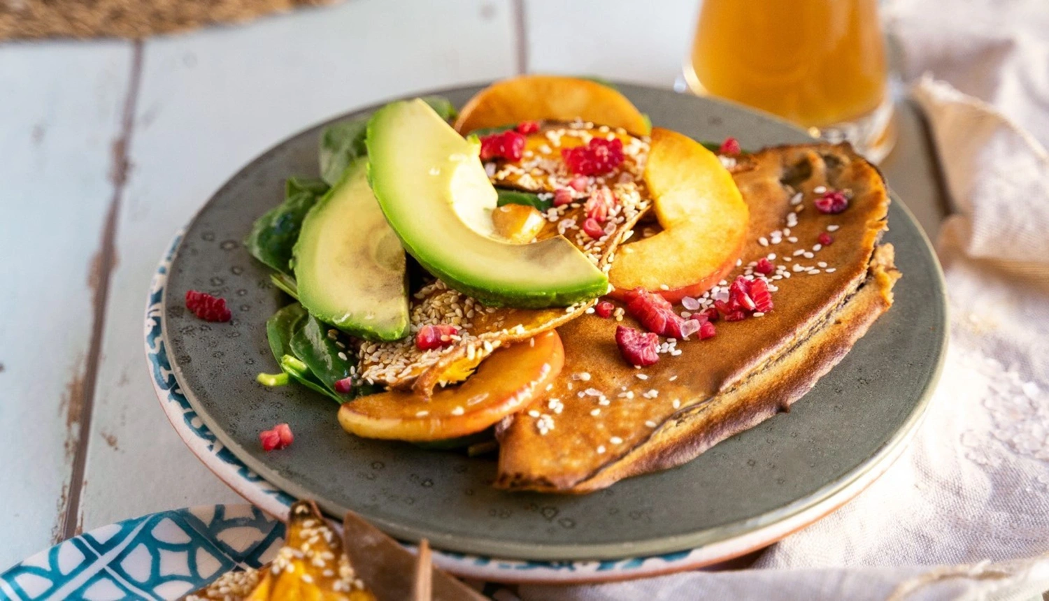 Eine gebratene Auberginenhälfte mit Avocado, Pfirsichscheiben, Spinat und Sesam belegt. Im Hintergrund steht ein Glas Saft.