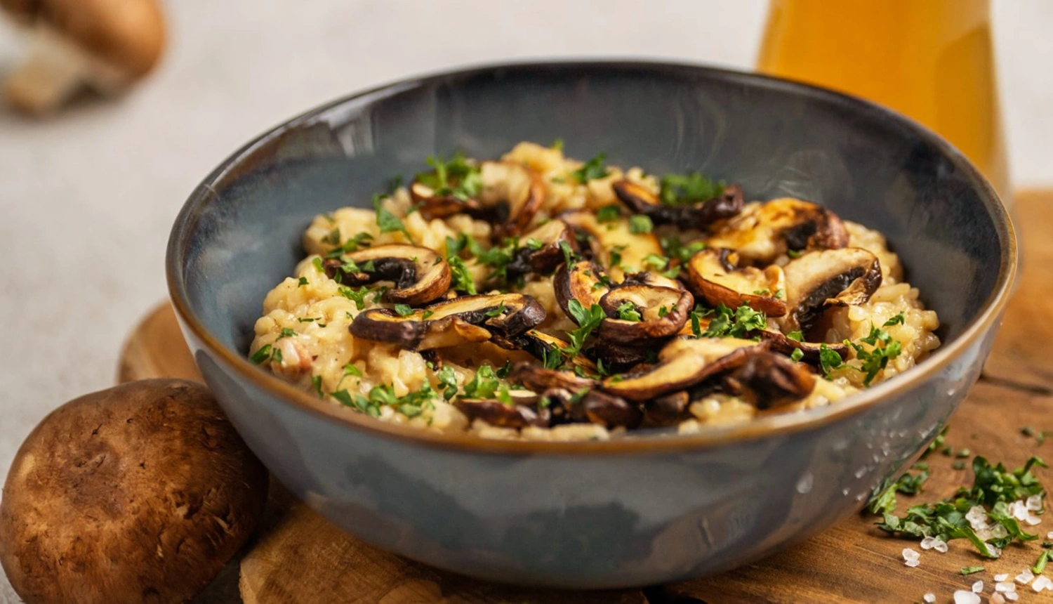 Eine Schüssel Risotto mit gebratenen Pilzen und gehackter Petersilie auf einem Holzbrett.