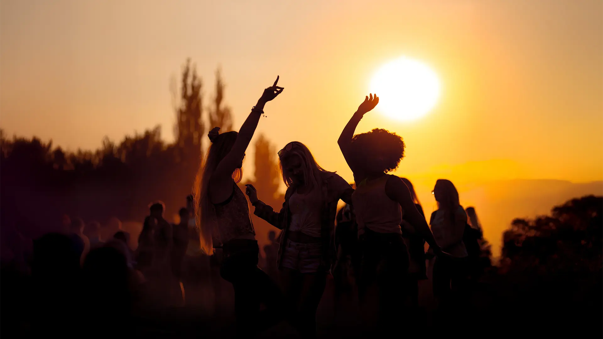 Vier junge Menschen tanzen untergehende Sonne im Hintergrund bei einem Festival.