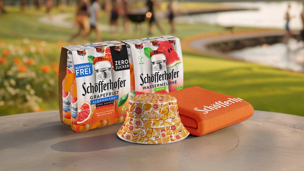 2 Schoefferhofer Weizen MIx Sechserpacks stehen auf einem Tisch, davor liegen eine Mütze und ein Handtuch.